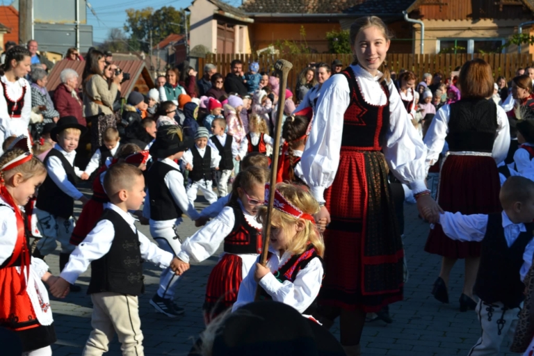 Kinder und Erwachsene tanzen bei einem Fest in traditioneller Kleidung auf einem Dorfplatz.